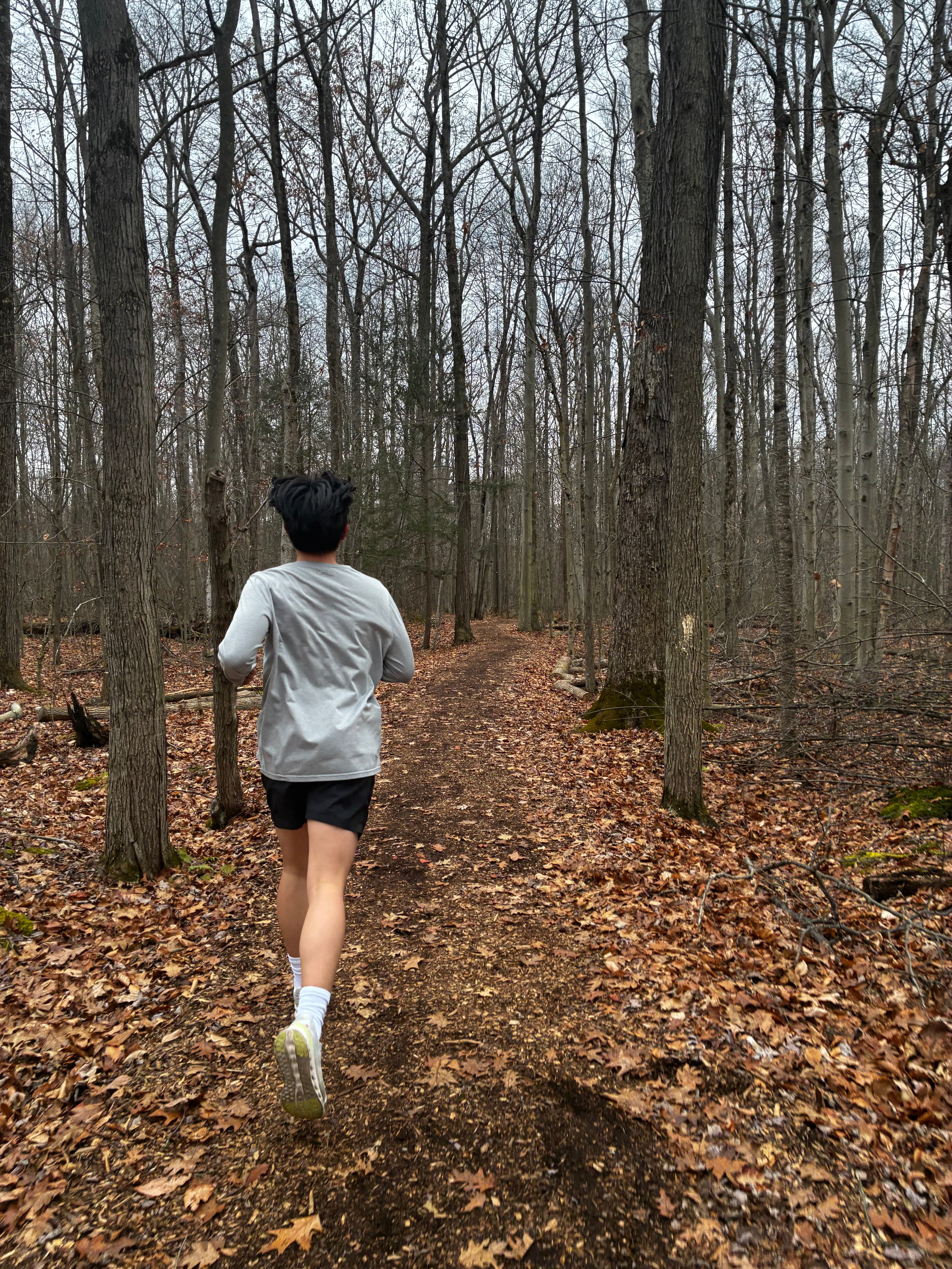 Jinho running down a leaf-covered trail through bare woods